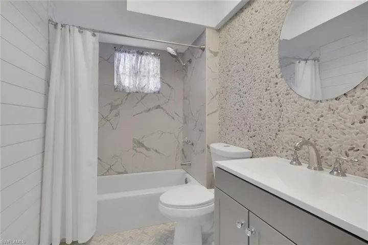 Bathroom featuring a pebble-textured accent wall, vanity with an integrated basin, shiplap wall paneling, shower-tub combination with large-format veined wall tile, and herringbone-patterned floor tile