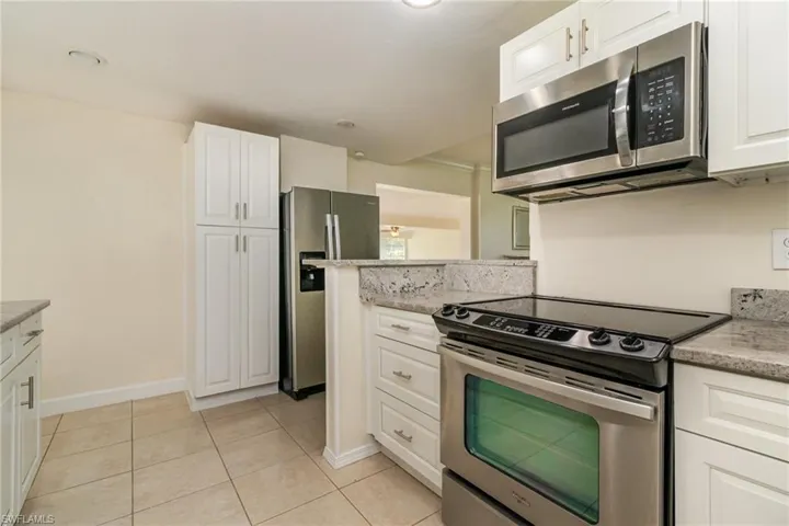 Kitchen with white cabinetry, stainless steel appliances, baseboards, light tile patterned flooring, and light stone countertops
