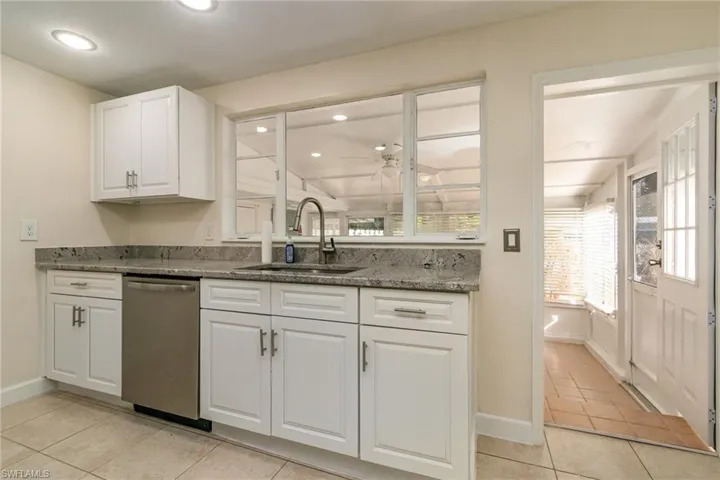 Kitchen featuring stainless steel dishwasher, a sink, stone counters, ceiling fan, and white cabinets