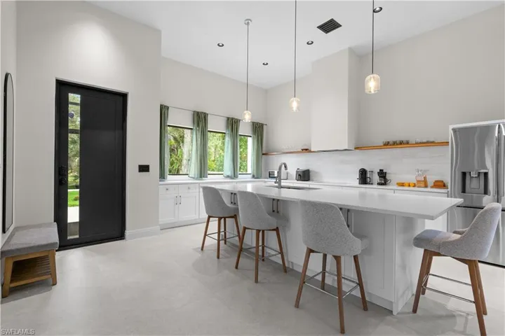 Kitchen featuring white cabinetry, a kitchen island with sink, a kitchen breakfast bar, stainless steel refrigerator with ice dispenser, and pendant lighting