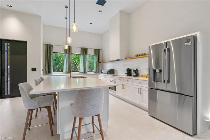 Kitchen featuring white cabinets, appliances with stainless steel finishes, hanging light fixtures, a breakfast bar area, and an island with sink
