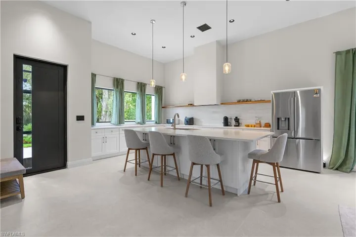 Kitchen featuring stainless steel refrigerator with ice dispenser, a kitchen island with sink, a kitchen breakfast bar, pendant lighting, and white cabinets