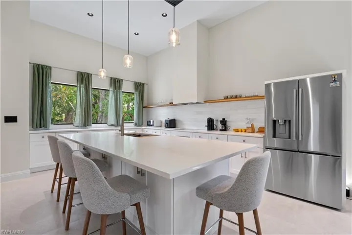 Kitchen with stainless steel refrigerator with ice dispenser, a breakfast bar, pendant lighting, a kitchen island with sink, and white cabinets