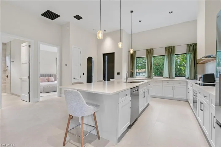 Kitchen with white cabinetry, a breakfast bar, a center island with sink, arched walkways, and hanging light fixtures