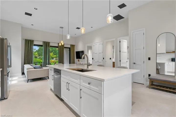 Kitchen featuring an island with sink, open floor plan, stainless steel appliances, white cabinetry, and decorative light fixtures