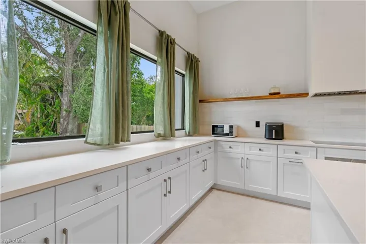 Kitchen with white cabinetry, open shelves, backsplash, and black appliances