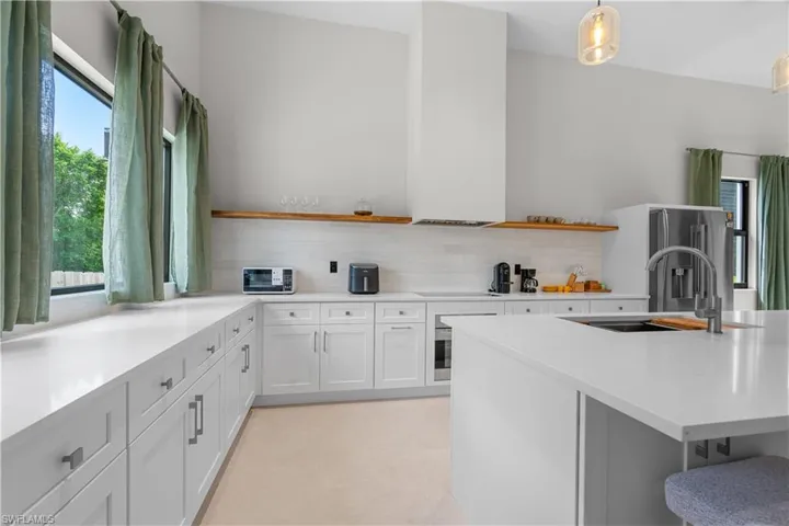 Kitchen featuring open shelves, white cabinets, stainless steel fridge, and light stone counters
