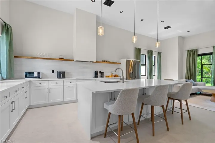 Kitchen with white cabinets, open shelves, decorative light fixtures, a kitchen breakfast bar, and backsplash