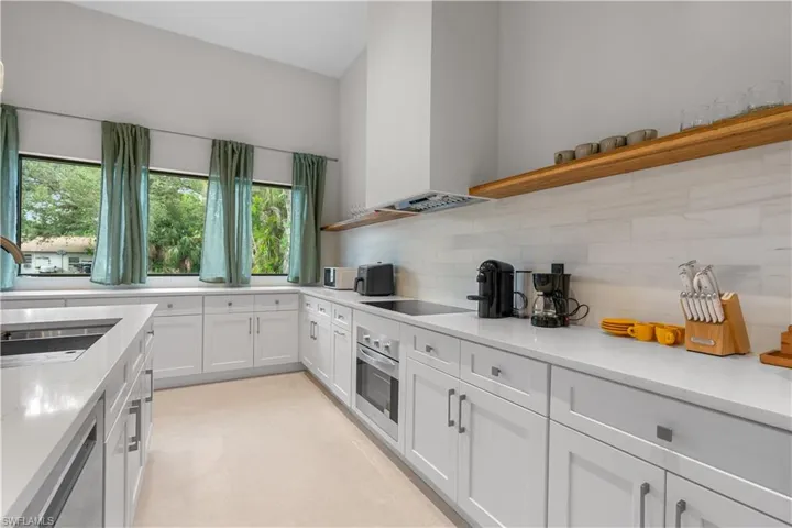 Kitchen featuring open shelves, white cabinets, light stone counters, custom range hood, and oven