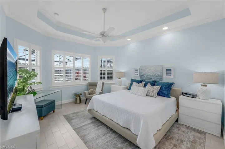 Bedroom with ceiling fan, light wood-type flooring, ornamental molding, and a tray ceiling