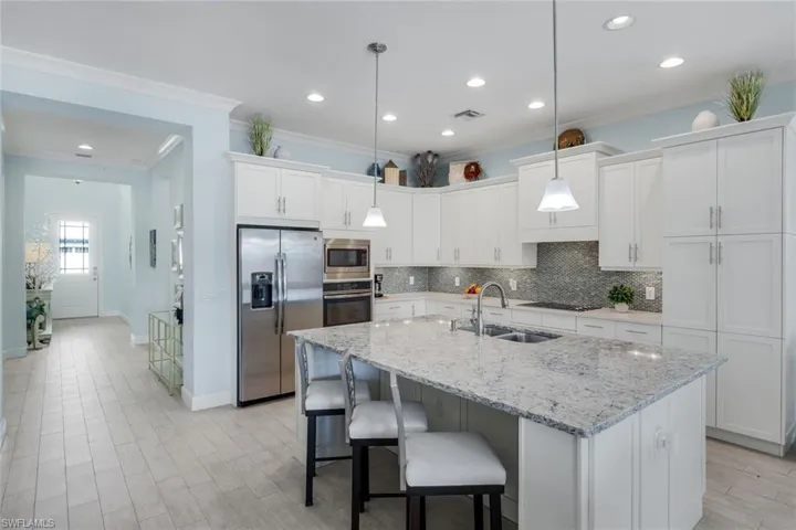 Kitchen with stainless steel appliances, white cabinets, decorative backsplash, light stone countertops, and hanging light fixtures