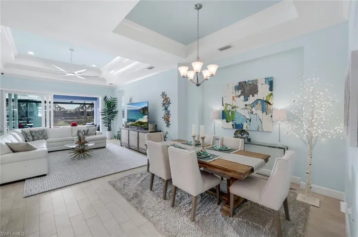 Dining room featuring light wood-style flooring, a tray ceiling, a ceiling fan, suspended lighting, and ornamental molding