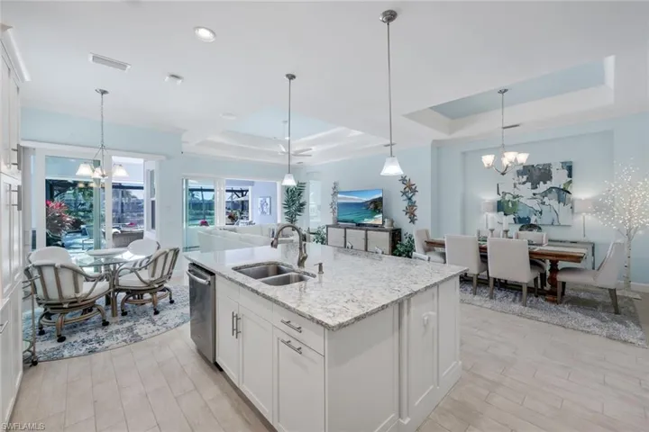 Kitchen featuring hanging lights, white cabinetry, a tray ceiling, an island with sink, and light stone countertops