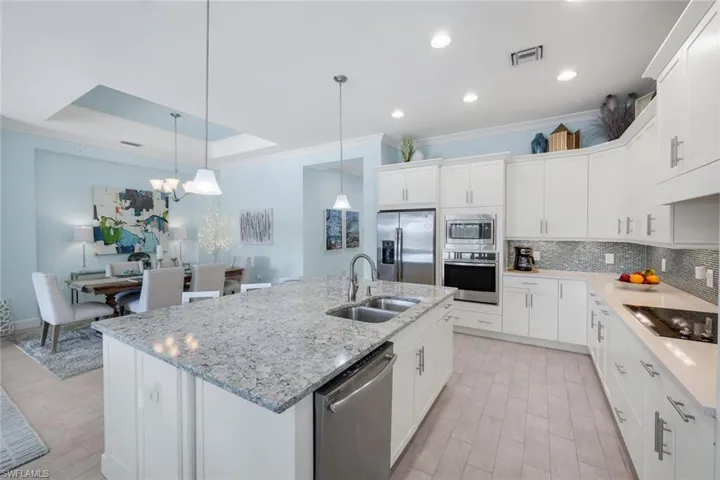 Kitchen with white cabinetry, stainless steel appliances, light stone countertops, decorative backsplash, and light wood finished floors