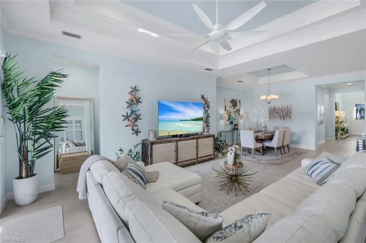 Living area featuring a ceiling fan, a raised ceiling, wood finished floors, ornamental molding, and a chandelier