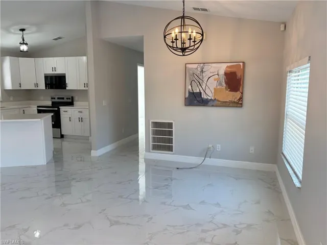 Kitchen with lofted ceiling, white cabinetry, stainless steel electric range oven, a notable chandelier, and pendant lighting