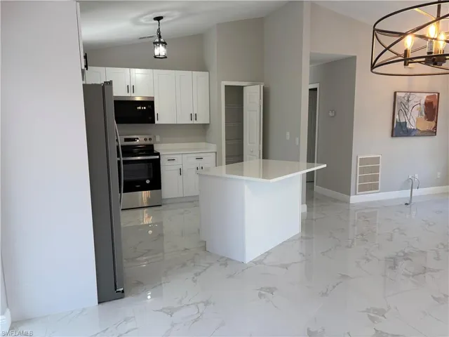 Kitchen with vaulted ceiling, pendant lighting, white cabinets, a center island, and stainless steel appliances