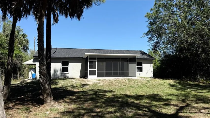 Back of property featuring stucco siding, a lawn, roof with shingles, and a sunroom