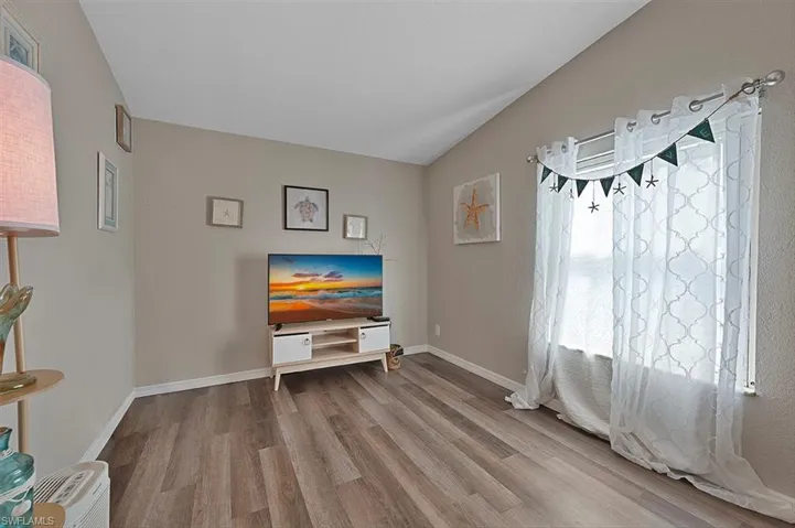 Living room featuring wood finished floors, lofted ceiling, and baseboards