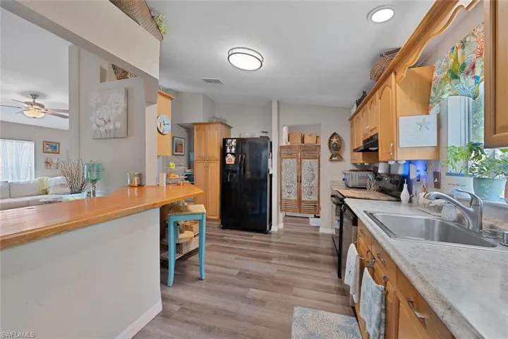 Kitchen with black appliances, a sink, under cabinet range hood, a ceiling fan, and light wood-type flooring