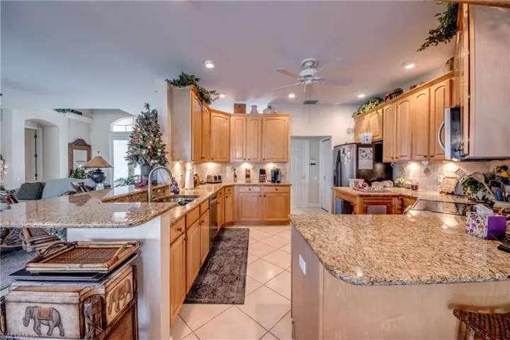 Kitchen with a peninsula, a kitchen breakfast bar, light stone countertops, open floor plan, and light wood finish cabinets