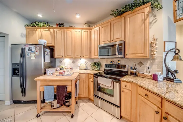 Kitchen with light wood finish cabinetry, stainless steel appliances, light stone countertops, and decorative backsplash