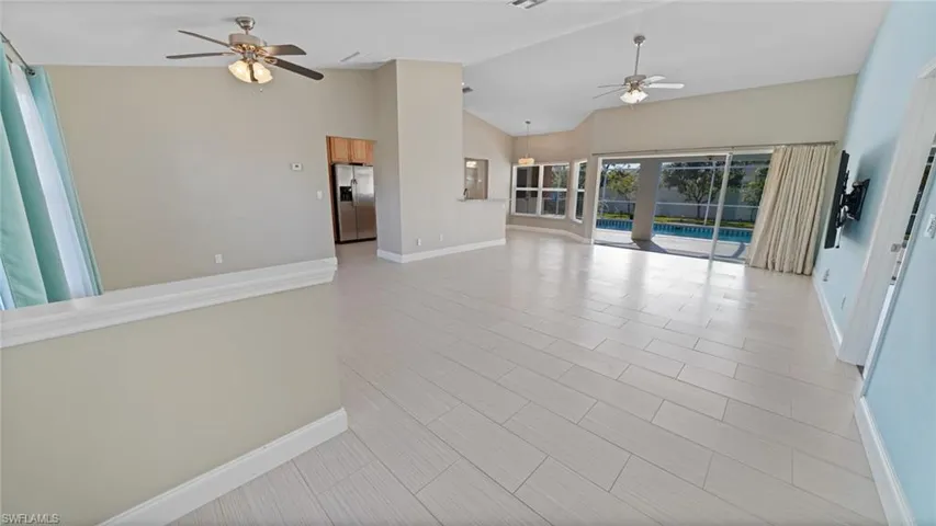Unfurnished living room with ceiling fans, cathedral ceiling, oversized triple sliders to under-truss pool deck area, and peek of breakfast nook with windows to pool deck