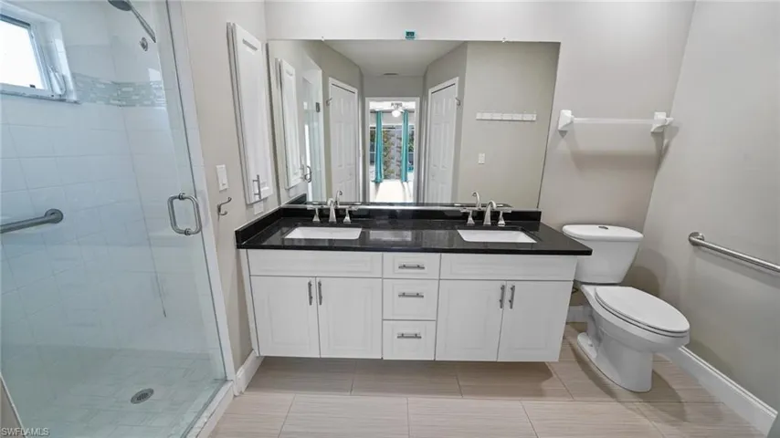 Bathroom featuring dual sink vanity with granite counter and tiled shower.