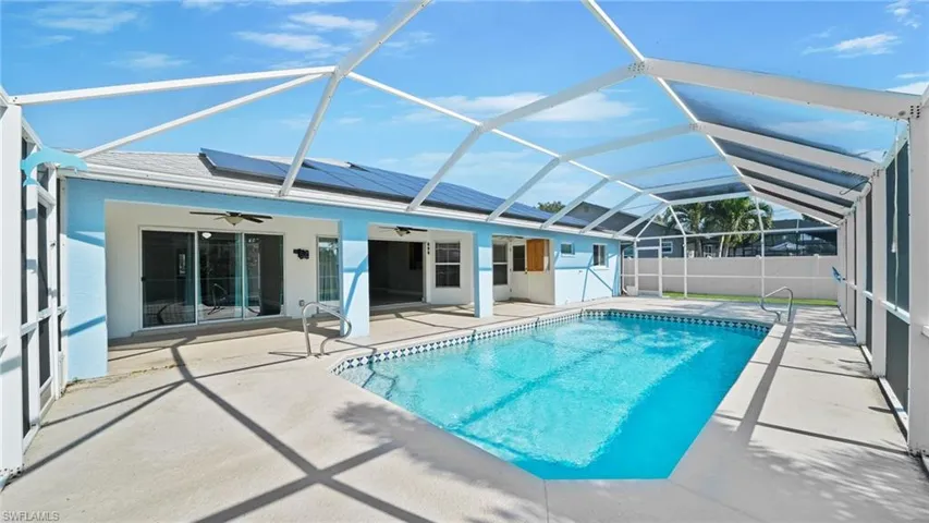 View of heated pool featuring mansard screen enclosure, under-truss deck, additional patio area, and oversized sliders to the living room