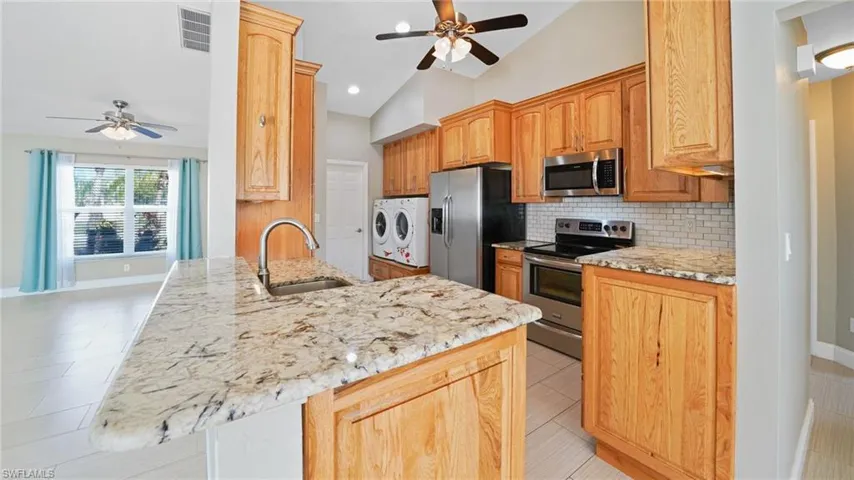 Kitchen with custom hickory cabinets & ganite counters, stainless steel appliances, vaulted ceiling, washer and clothes dryer, and stainless sink