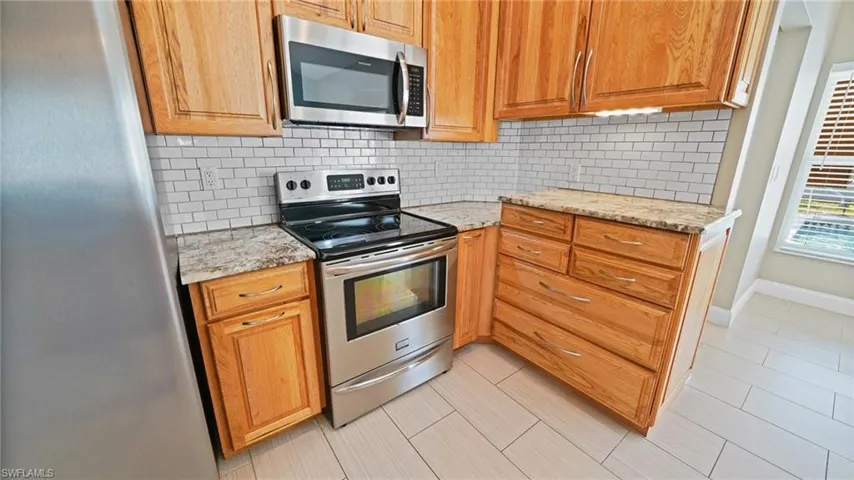 Kitchen featuring light tile floors, subway tile backsplash, stainless steel appliances, under-cabinet lighting, and granite counters