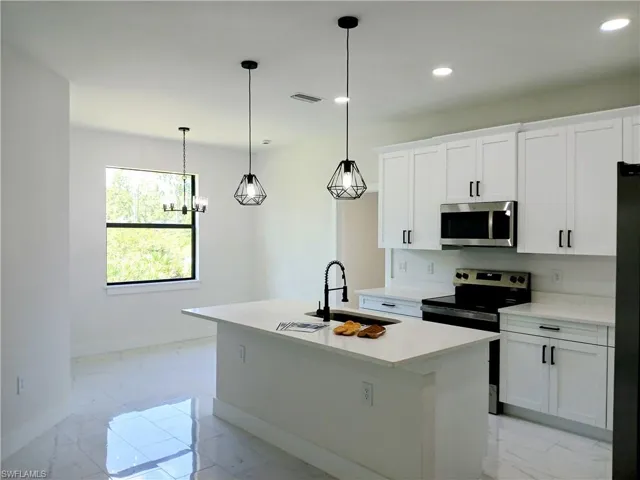 Kitchen featuring decorative light fixtures, stainless steel appliances, sink, light tile patterned floors, and a kitchen island with sink