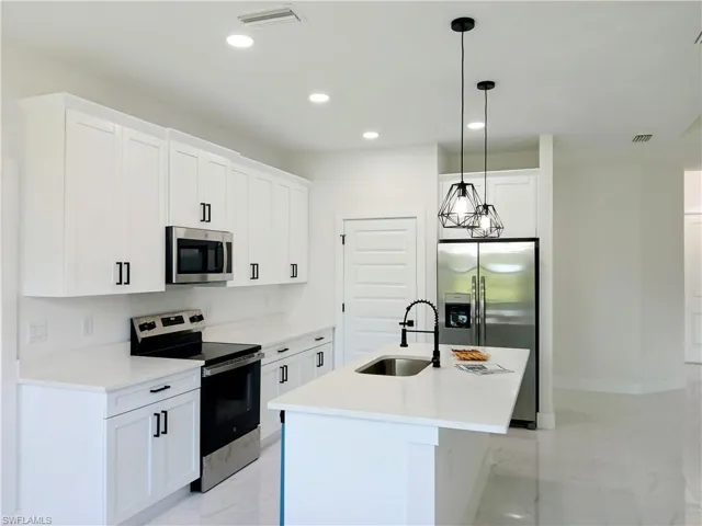 Kitchen with white cabinetry, stainless steel appliances, an island with sink, sink, and light tile patterned floors