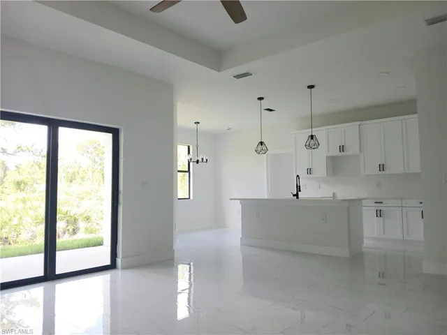 Kitchen with light tile patterned flooring, ceiling fan with notable chandelier, a healthy amount of sunlight, and a kitchen island with sink