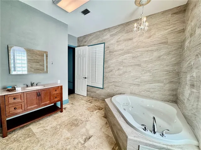 Full bath with vanity, a tub with jets, and a chandelier