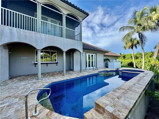 Back of property featuring an in-ground hot tub, a balcony, a tile roof, and stucco siding