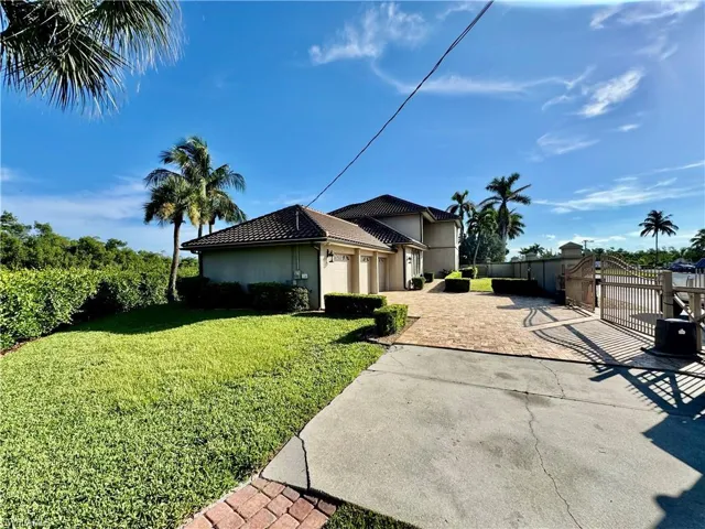 View of side of home with decorative driveway, a garage, a gate, stucco siding, and a tile roof