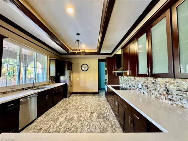 Kitchen with a tray ceiling, backsplash, stainless steel appliances, light countertops, and ornamental molding