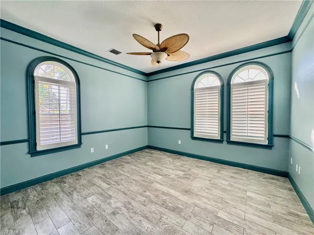 Empty room featuring plenty of natural light, a textured ceiling, a ceiling fan, wood finished floors, and ornamental molding