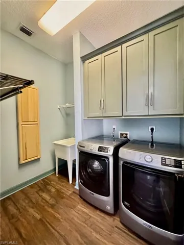 Laundry room featuring cabinet space, independent washer and dryer, a textured ceiling, and dark wood-style flooring