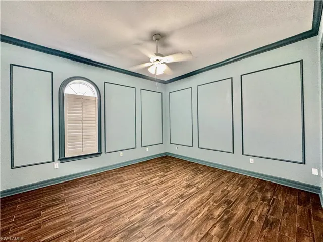 Empty room featuring a textured ceiling, dark wood-style flooring, ceiling fan, and ornamental molding