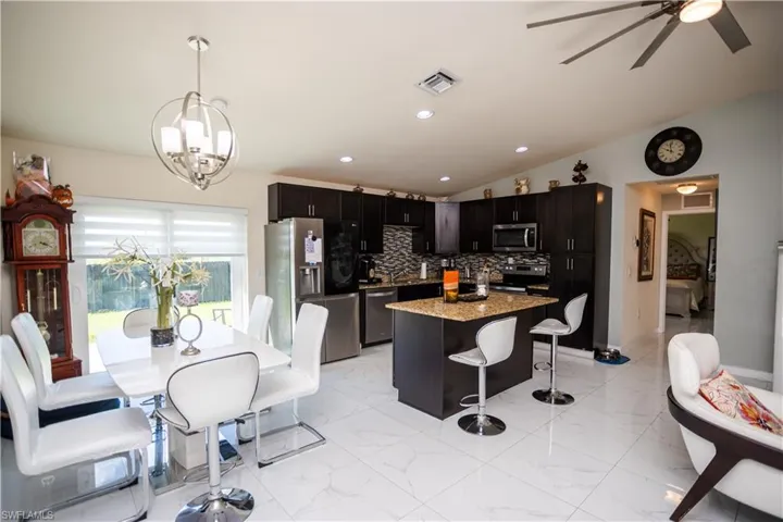 Open-concept kitchen and dining area featuring dark wood-finish cabinetry, stainless steel appliances, a kitchen island with seating, and large-format tile flooring