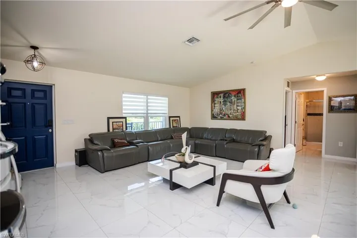 Open-concept living space with large format white tile flooring, vaulted ceilings, and a contemporary ceiling fan