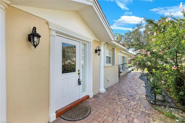 Stucco exterior with decorative outdoor lighting, an entry door featuring leaded glass, and a brick paver walkway bordered by lush landscaping