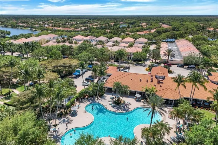 Expansive community grounds featuring a large swimming pool, mature palm trees, multiple residential buildings with terracotta roofs, and tennis courts