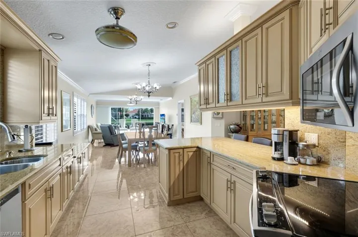 Kitchen featuring light-toned cabinetry with glass-front accents, stainless steel appliances, and polished stone-finish countertops