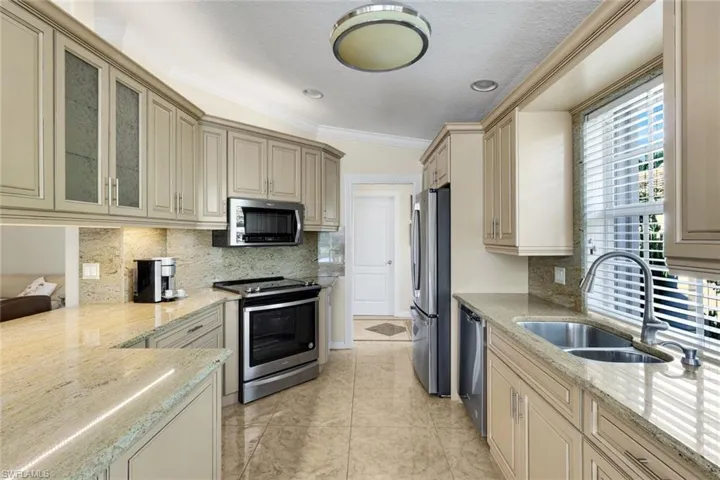 Galley kitchen with light-toned cabinetry, stainless steel appliances, granite countertops, and tile flooring