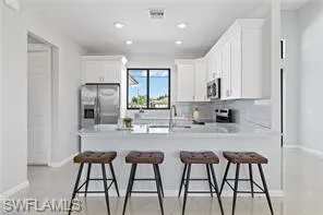 Kitchen featuring stainless steel appliances, kitchen peninsula, tasteful backsplash, and white cabinetry