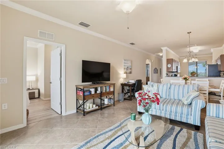 Living room with ornamental molding, arched walkways, light tile patterned floors, and a chandelier