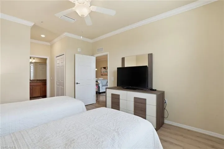 Bedroom with ornamental molding, light wood-style flooring, connected bathroom, ceiling fan, and a closet